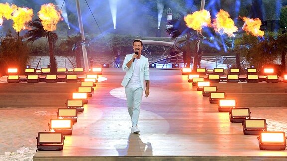 Florian Silbereisen in helltürkisfarbenem Anzug auf der Bühne, im Hintergrund Feuershow.