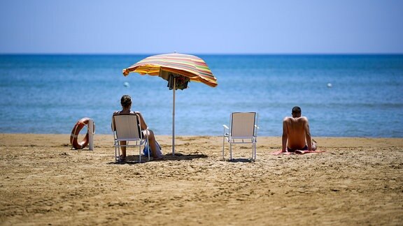 Touristen sitzen am Strand der Küstenstadt Porto Empedocle. 