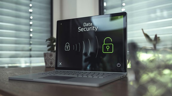 Laptop auf einem Tisch zeigt Sicherheitsicons, im Hintergrund geschlossene Rollläden