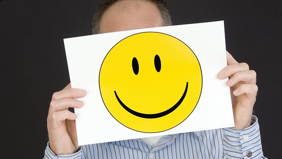 Mann hält sich einen Smiley vor das Gesicht
