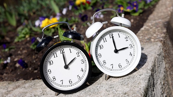 Ein Wecker zeigt zwei Uhr und der andere drei Uhr