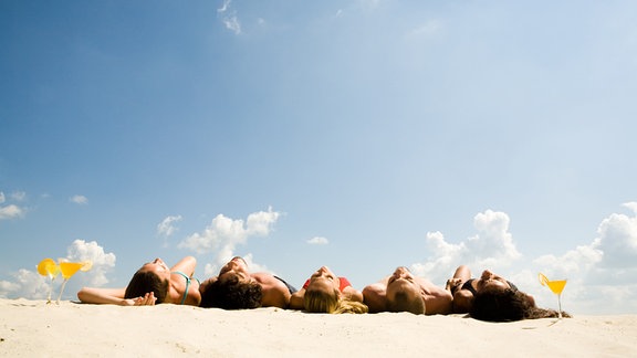 Fünf Teenager liegen beim Sonnenbaden auf dem Sand.