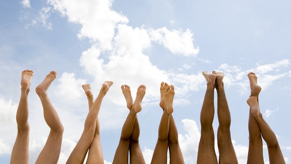 Die erhobenen Beine von 6 Personen vor sonnigem Himmel