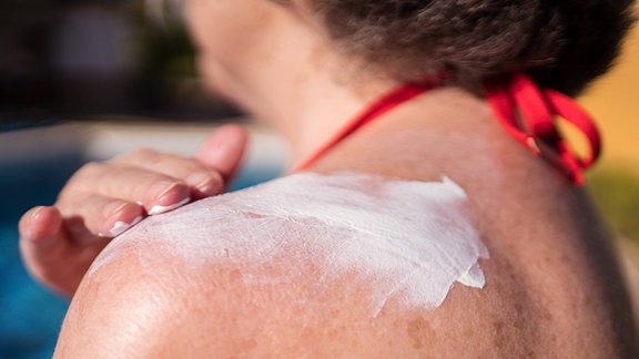 Seniorin trägt Sonnenschutz auf ihre Haut auf.