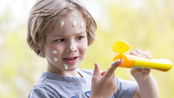 Kleiner Junge trägt sich selber Sonnencreme im Gesicht auf