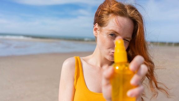 Rothaarige Frau zeigt im Urlaub Sprühflasche am Strand