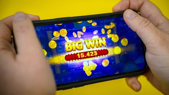 Eine Person hält ein Smartphone in den Händen, auf dem ein Online-Glücksspiel geöffnet ist.