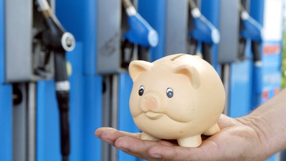 Sparschwein auf einer Hand vor einer Zapfsäule
