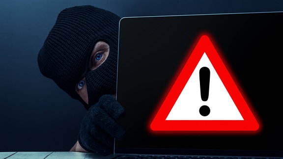 Mann mit Skimaske hinter einem Laptop