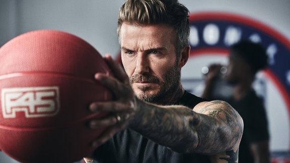 David Beckham hält einen Ball.