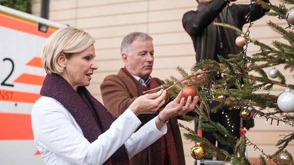 Szene aus der Serie "In aller Freundschaft" in der drei ProtagonistInnen einen Weihnachtsbaum schmücken.