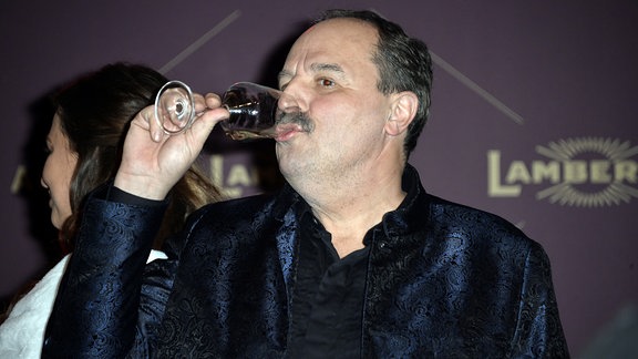 Johann Lafer trinkt aus einem Glas.
