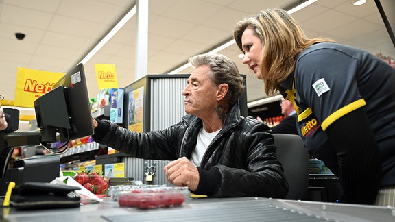 Der deutsche Rockmusiker Peter Maffay arbeitet an der Kasse eines Netto-Supermarktes und wird von einer Kassiererin unterstützt. 