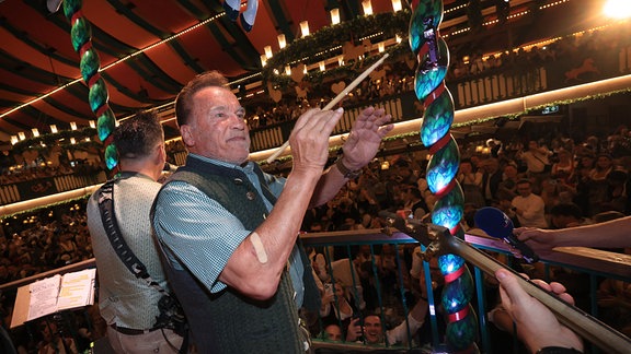 Arnold Schwarzenegger, Schauspieler, dirigiert im Marstall-Festzelt auf der Bühne. Die Wiesn findet vom 21. September bis 6. Oktober 2024 statt.