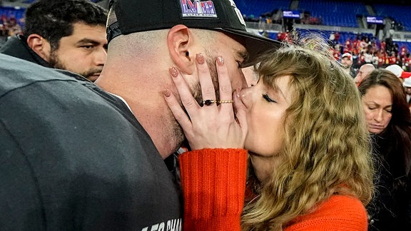 Die Musikerin Taylor Swift (r) küsst Kansas City Chiefs Tight End Travis Kelce nach dem NFL-Footballspiel auf dem Spielfeld. 