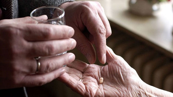 Eine Hand legt einer Zweiten Tabletten in die Hand