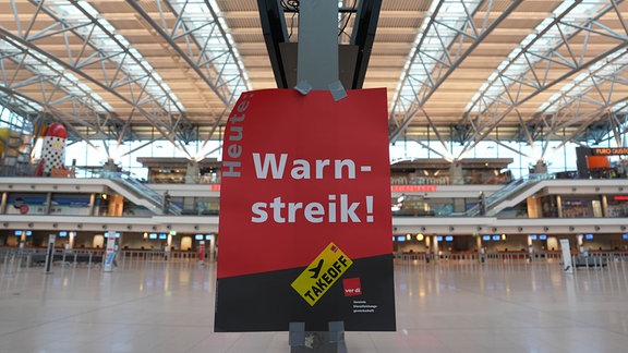 Ein Schild mit der Aufschrift „Warnstreik!“ hängt im Terminal eines Flughafens.