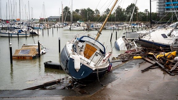 Beschädigte Schiffe liegen im Hafen nach einer Sturmflut auf einem Anleger und im Wasser.
