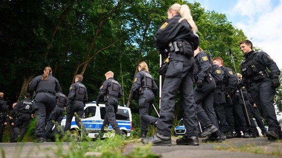 Polizisten sind mit Suchstangen auf der Suche nach einer vermissten Grundschülerin an einem Waldstück unterwegs.