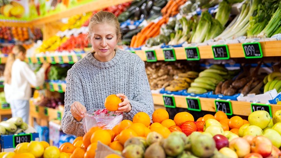 Eine Frau packt im Supermarkt Orangen ein.