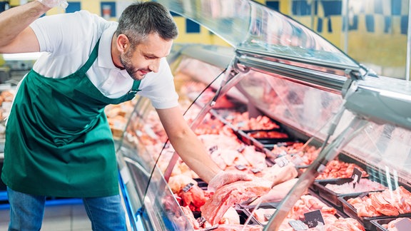Ein Mann nimmt ein Stück Fleisch aus der Theke im Supermarkt.