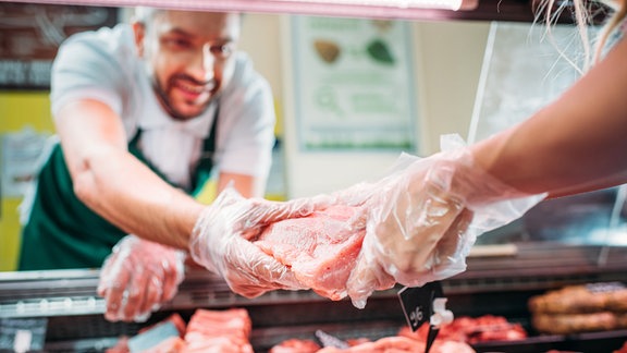 Ein Mann nimmt ein Stück Fleisch aus der Theke im Supermarkt.