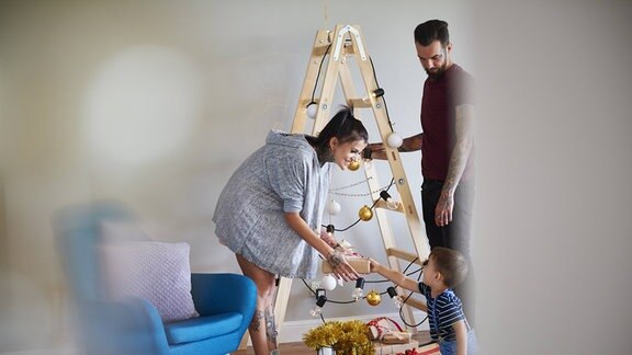 Eine Familie schmückt eine Leiter wie einen Tannenbaum