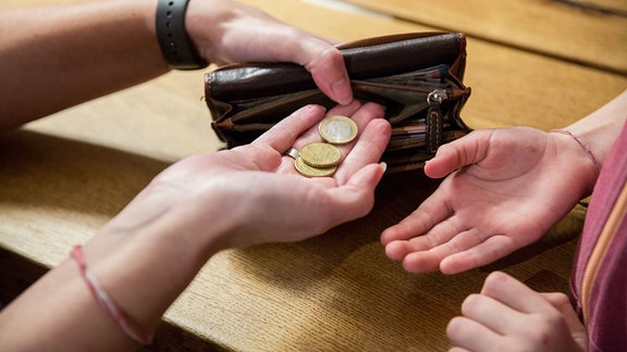 Ein Kind bekommt von der Mutter, die eine Geldbörse in den Händen hält, Ihr Taschengeld auf die Hand.