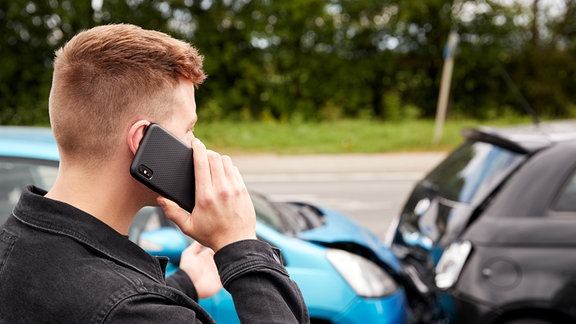 Ein Mann telefoniert nach einem Verkehrsunfall