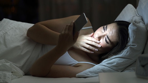 Besorgte Frau findet nachts auf dem Bett zu Hause mit dunklem Hintergrund schlechte Nachrichten in einem Smartphone.
