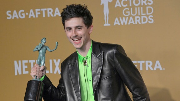 Timothée Chalamet lächet mit einer Trophäe in der Hand