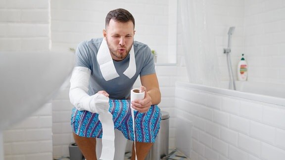 Inszenierters Foto eines junges Mannes mit angestrengtem Gesicht der auf der Toilette sitzt.