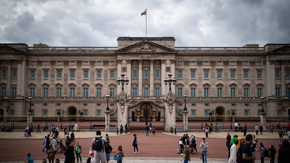 Touristen stehen vor den Toren vom Buckingham Palast. 
