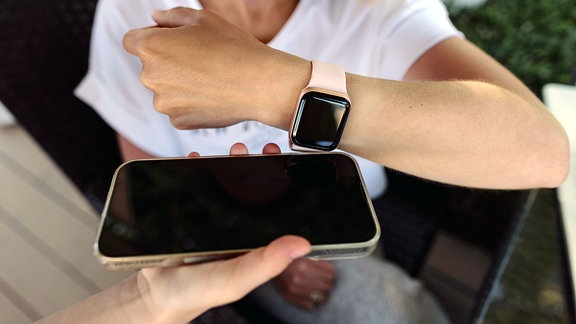 Frau bezahlt kontaktlos mit Smartwatch auf dem von der Kassiererin gehaltenen Mobiltelefon.