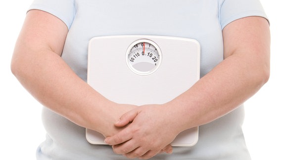 Frau hält sich eine Waage vor den Bauch