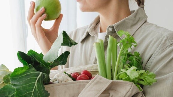 Frau hält wiederverwendbaren Beutel voller Bio-Gemüse und Obst.