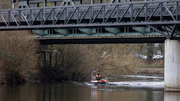 Feuerwehrleute fahren mit einem Boot die Lahn ab und suchen an eine Brücke.