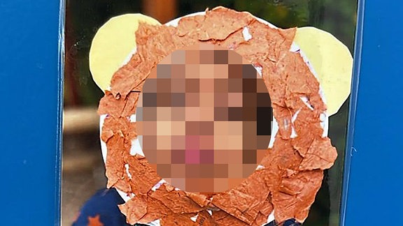 Ein Junge schaut durch eine Löwemähne aus Pappe.
