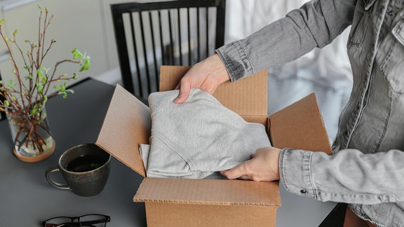 Eine Frau packt Kleidung in einen Karton.