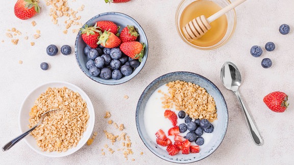 Blick von oben auf einen Tisch zeigt Schalen mit Beeren, Müsli und Honig. 