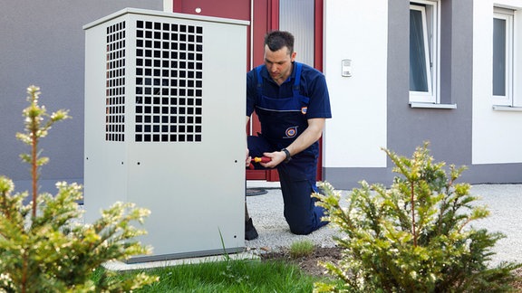 Ein Heizungsmonteur montiert das Gehäuse für eine Wärmepumpe.