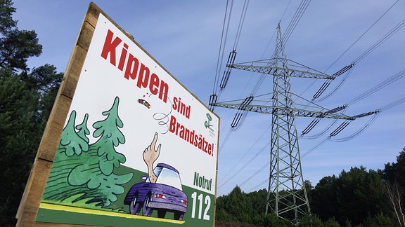 Vor einem Starkstrommast steht ein Schild zur Waldbrandgefahr.