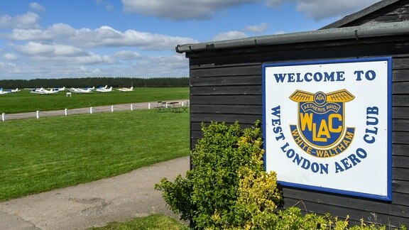 Auf einem Sportplatz steht eine Hütte mit einem Zeichen mit der Aufschrift "West London Aero Club"