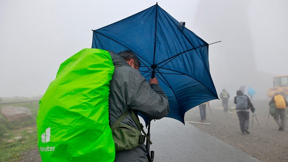 Mit einem Regenschirm ist ein Wanderer auf dem Brocken unterwegs.