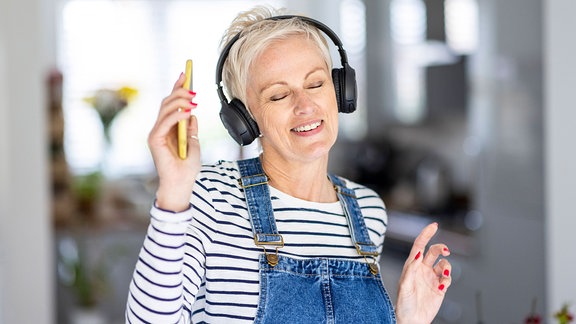 Reife Frau tanzt, während sie zu Hause Musik hört.