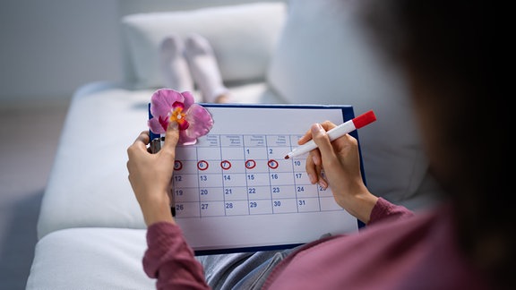 Symbolbild: Eine Frau kreist Tage am Kalender rot ein.