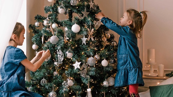 Zwei Mädchen dekorieren einen Weihnachtsbaum