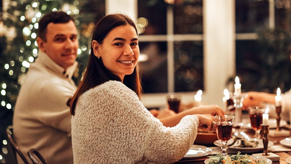 Glückliches junges Familienpaar lächelt in die Kamera, während es am Tisch sitzt und das Weihnachtsessen genießt.