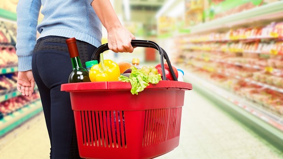 Eine Frau hält einen vollen Einkaufskorb im Supermarkt