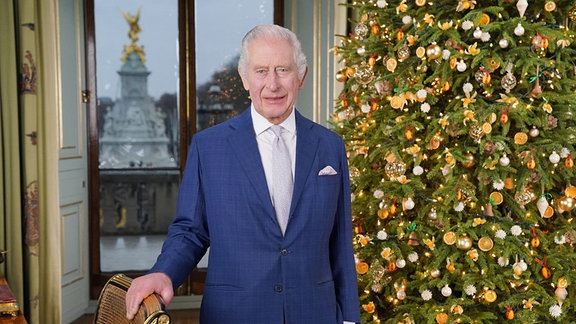 Der britische König Charles III. steht während der Aufzeichnung seiner Weihnachtsbotschaft im Buckingham Palace neben einer weihnachtlich geschmückten Tanne.